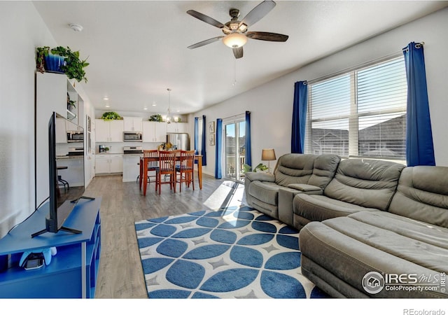 living room with ceiling fan with notable chandelier and light hardwood / wood-style flooring