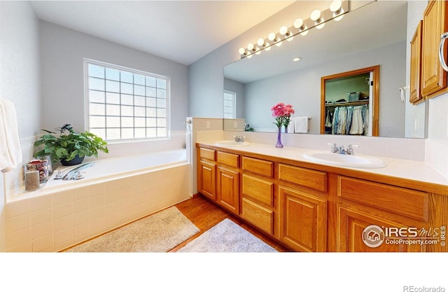 bathroom with hardwood / wood-style flooring, vanity, and tiled tub