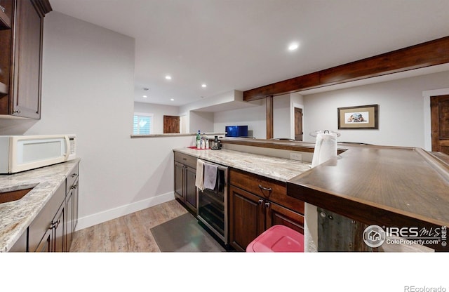 kitchen with wine cooler, light stone counters, light wood-type flooring, and dark brown cabinetry