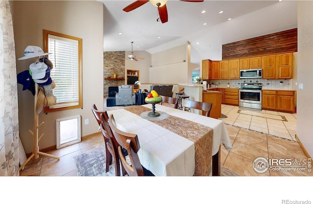 tiled dining room featuring ceiling fan, a stone fireplace, and high vaulted ceiling