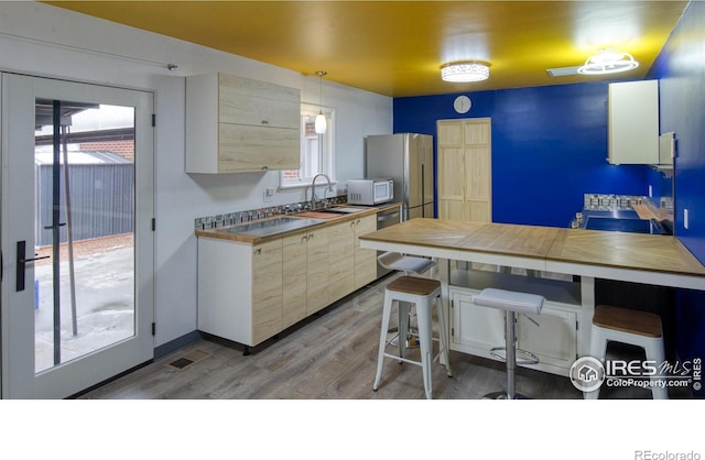 kitchen with wooden counters, light hardwood / wood-style floors, hanging light fixtures, sink, and white appliances