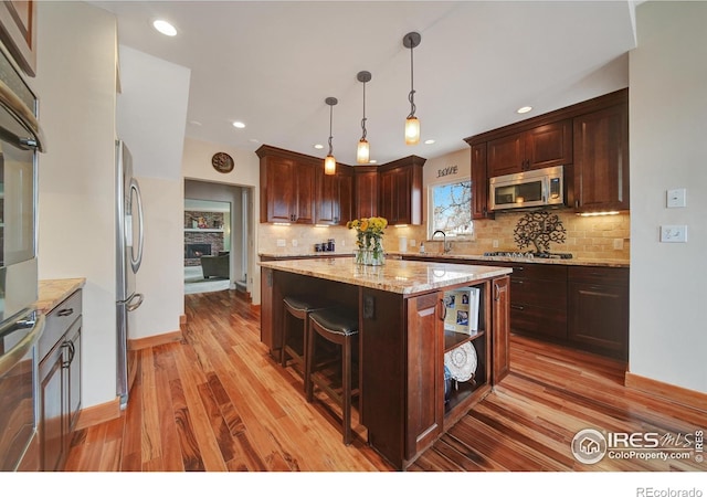 kitchen with light stone counters, pendant lighting, stainless steel appliances, a center island, and light hardwood / wood-style floors