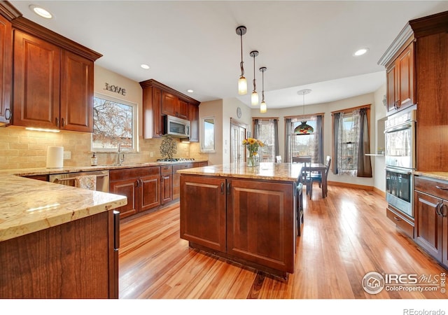 kitchen featuring light wood-type flooring, tasteful backsplash, a kitchen island, stainless steel appliances, and decorative light fixtures