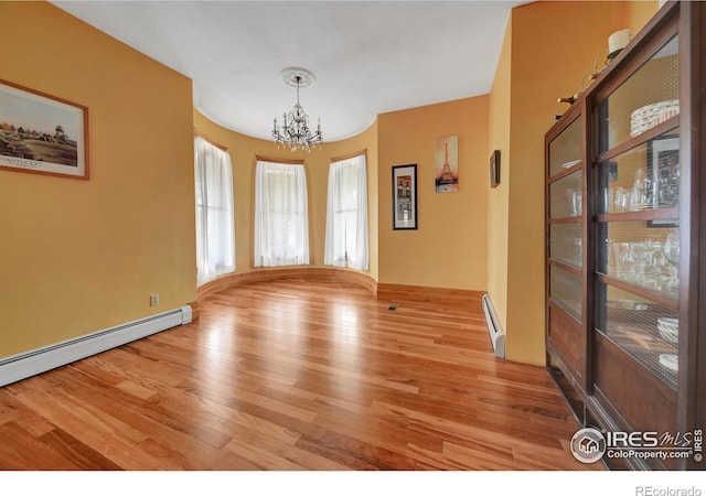 unfurnished room with light wood-type flooring, a baseboard heating unit, and a chandelier