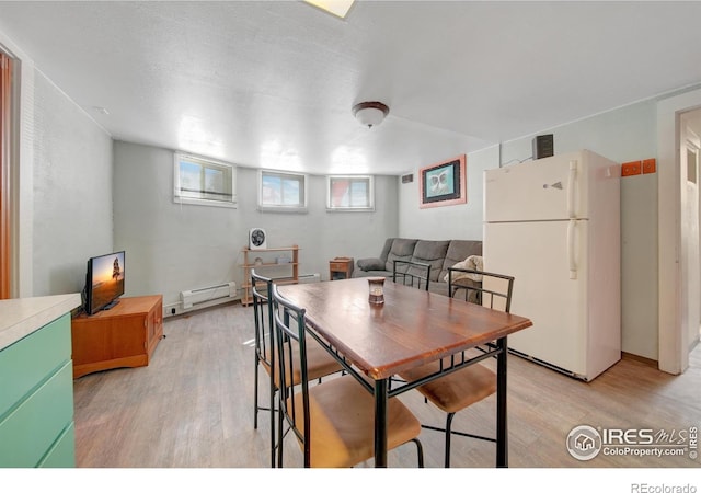 dining space with a baseboard radiator, light hardwood / wood-style flooring, and a textured ceiling