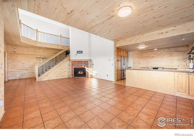 unfurnished living room featuring a high ceiling, wood ceiling, wood walls, light tile patterned floors, and a tiled fireplace