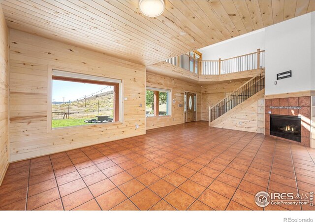 unfurnished living room with a fireplace, wood ceiling, tile patterned floors, and wooden walls