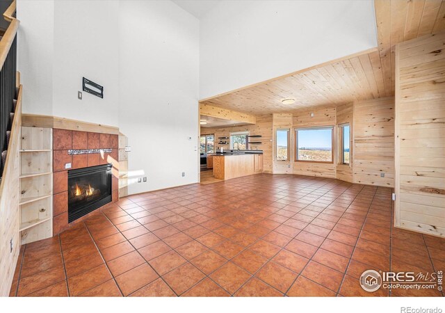 unfurnished living room featuring a tile fireplace, wood walls, sink, a high ceiling, and wood ceiling