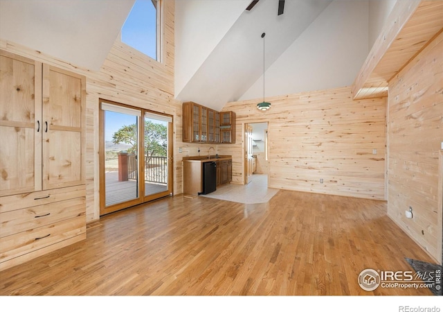 unfurnished living room with light hardwood / wood-style floors, wooden walls, ceiling fan, high vaulted ceiling, and sink