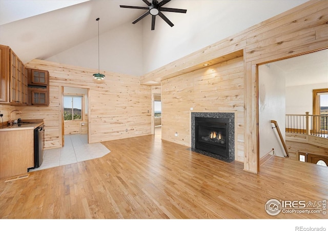 living room featuring ceiling fan, light wood-type flooring, sink, and wooden walls