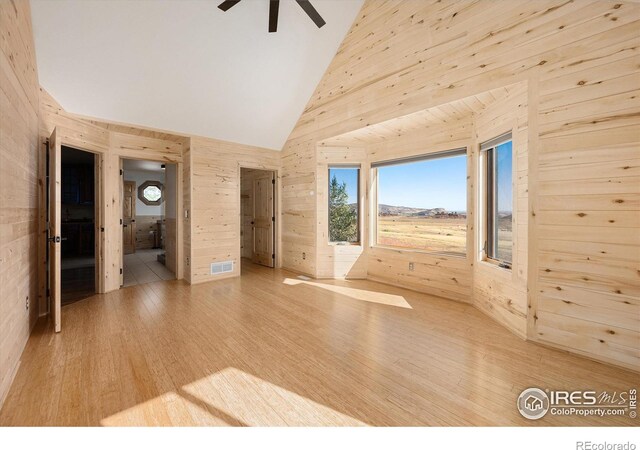 interior space with high vaulted ceiling, ceiling fan, wooden walls, and light hardwood / wood-style flooring