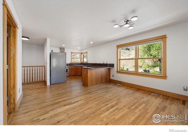 kitchen with light wood-type flooring, stainless steel fridge, kitchen peninsula, and a healthy amount of sunlight