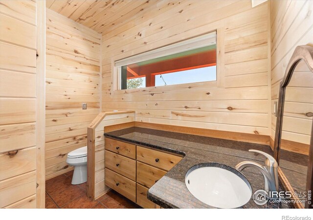 bathroom with tile patterned floors, toilet, vanity, and wood walls