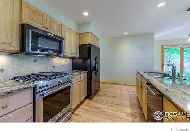 kitchen featuring sink, tasteful backsplash, light hardwood / wood-style flooring, black appliances, and light stone countertops