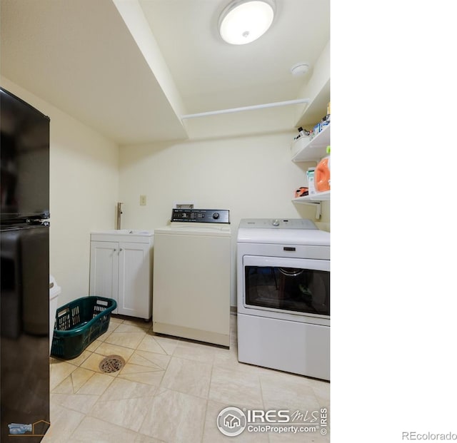 clothes washing area featuring sink, washing machine and clothes dryer, and cabinets