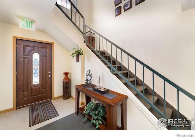 carpeted foyer featuring a textured ceiling and vaulted ceiling