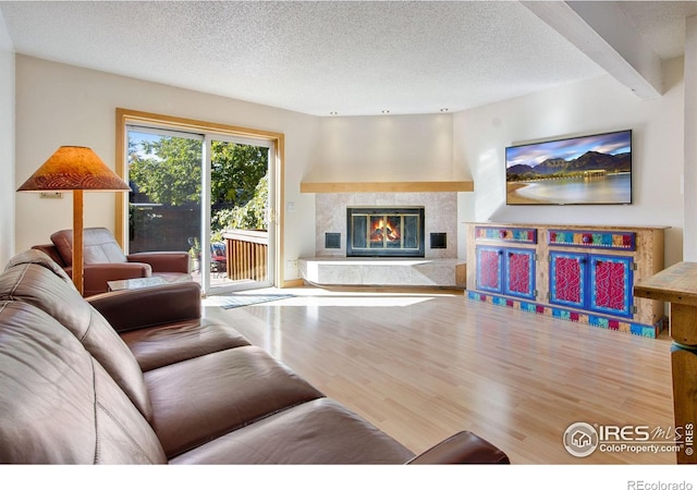 living room with wood-type flooring, a textured ceiling, beam ceiling, and a tile fireplace