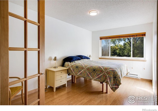 bedroom featuring light hardwood / wood-style floors, a textured ceiling, and a baseboard radiator