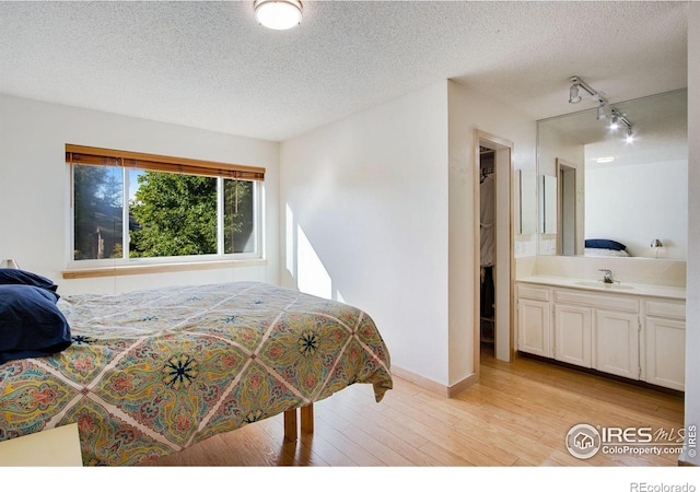 bedroom with sink, connected bathroom, light hardwood / wood-style floors, and a textured ceiling