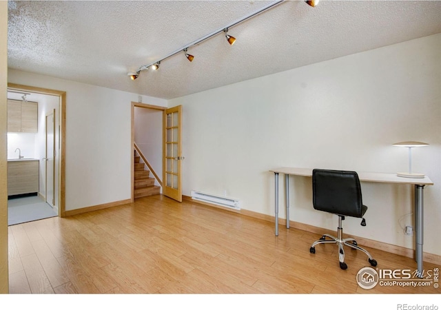 unfurnished office featuring sink, baseboard heating, hardwood / wood-style flooring, and a textured ceiling