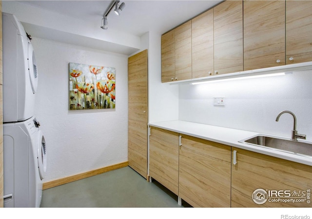 laundry room featuring cabinets, stacked washer / dryer, and sink