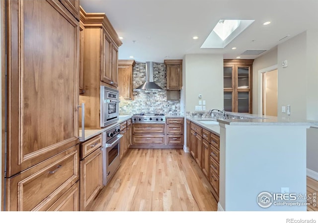 kitchen with sink, kitchen peninsula, light hardwood / wood-style flooring, wall chimney exhaust hood, and stainless steel appliances