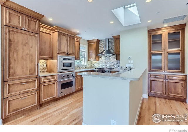 kitchen with light hardwood / wood-style floors, wall chimney exhaust hood, stainless steel appliances, and tasteful backsplash