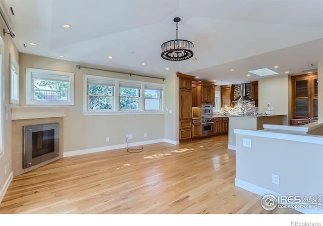 kitchen with a chandelier, wall chimney range hood, light hardwood / wood-style flooring, decorative backsplash, and oven