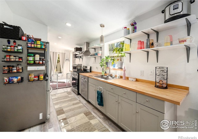 kitchen featuring recessed lighting, butcher block countertops, wall chimney range hood, open shelves, and appliances with stainless steel finishes