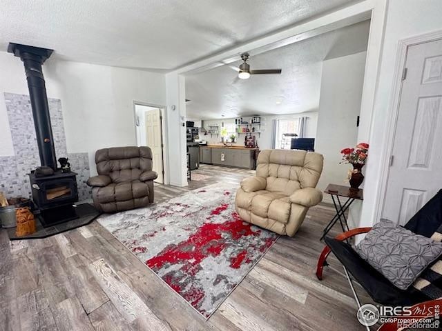 living area featuring a textured ceiling, wood finished floors, a wood stove, and a ceiling fan
