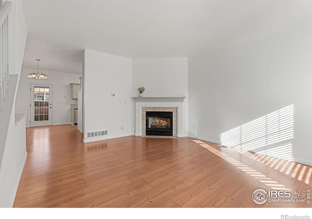 unfurnished living room with light wood-type flooring, a tile fireplace, and an inviting chandelier