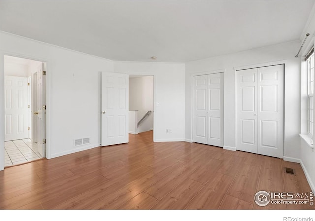 unfurnished bedroom featuring light hardwood / wood-style floors and two closets