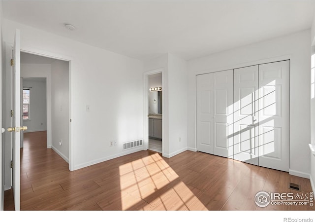 unfurnished bedroom with hardwood / wood-style flooring, ensuite bath, and a closet