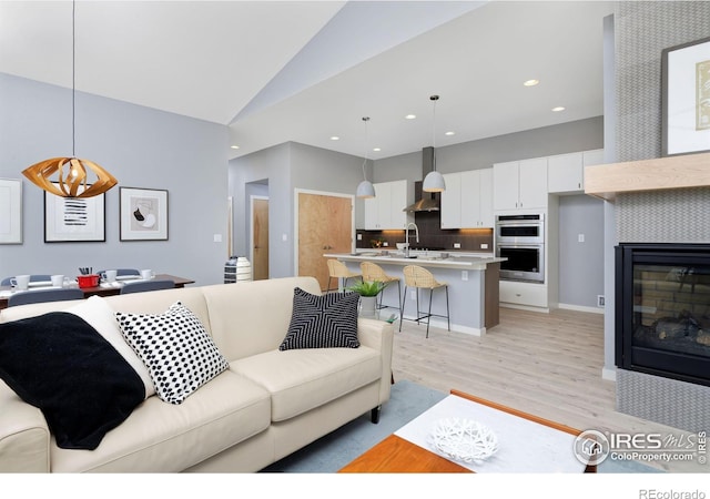 living room featuring light hardwood / wood-style floors, a fireplace, lofted ceiling, and sink