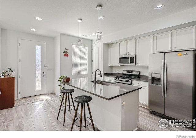 kitchen featuring white cabinets, pendant lighting, stainless steel appliances, light hardwood / wood-style flooring, and sink