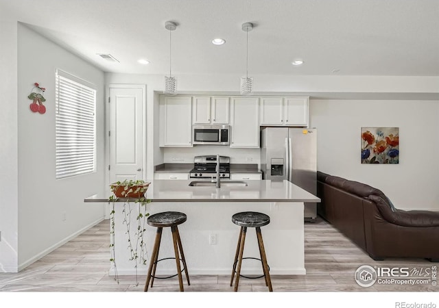 kitchen with white cabinets, a kitchen island with sink, stainless steel appliances, and decorative light fixtures