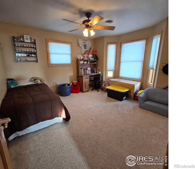 bedroom featuring ceiling fan, a textured ceiling, multiple windows, and carpet floors