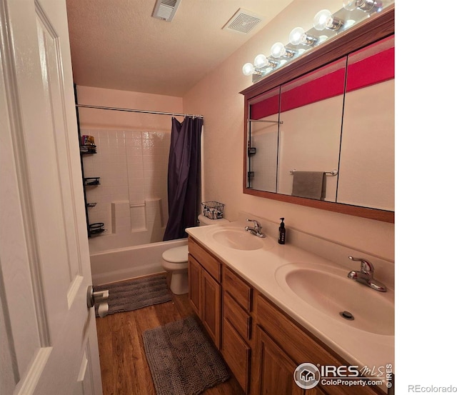 full bathroom with a textured ceiling, hardwood / wood-style flooring, toilet, shower / bath combo with shower curtain, and vanity