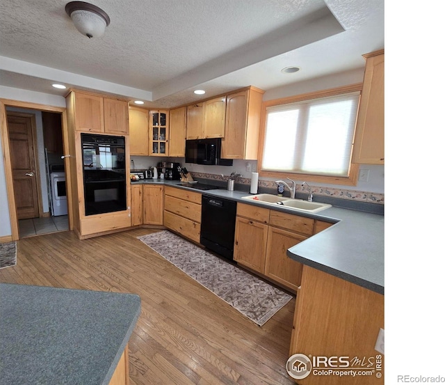 kitchen with black appliances, sink, a textured ceiling, a tray ceiling, and light hardwood / wood-style floors