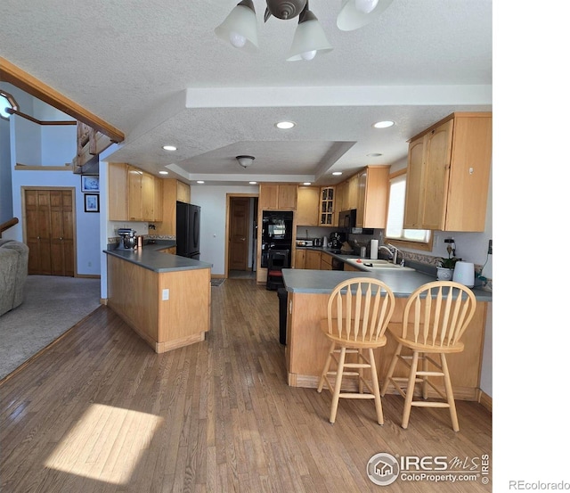 kitchen with kitchen peninsula, a textured ceiling, black appliances, dark wood-type flooring, and sink