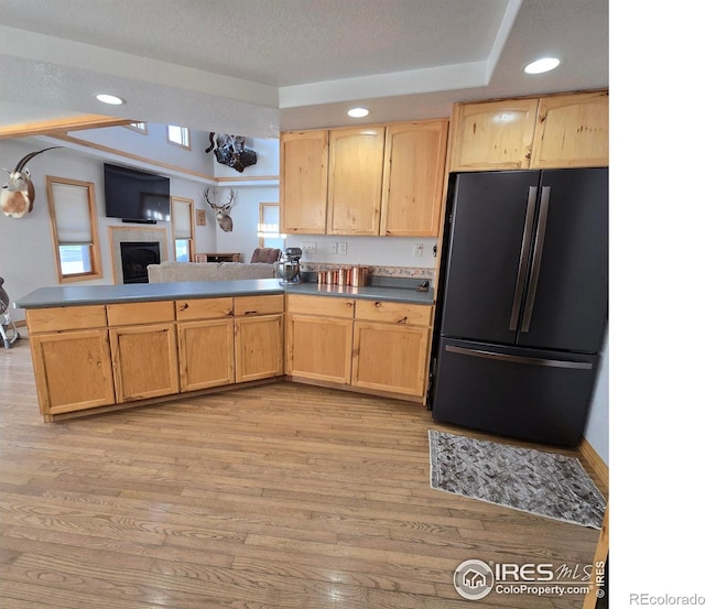 kitchen with light brown cabinetry, black refrigerator, a textured ceiling, and light wood-type flooring