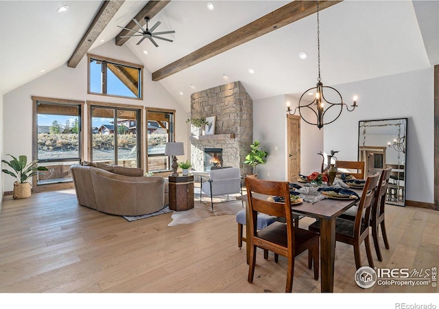 dining area with beam ceiling, light hardwood / wood-style flooring, high vaulted ceiling, a fireplace, and ceiling fan with notable chandelier