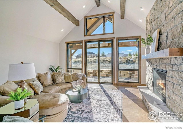 living room featuring light hardwood / wood-style floors, a stone fireplace, beam ceiling, and high vaulted ceiling