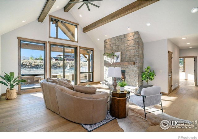 living room with a stone fireplace, light hardwood / wood-style flooring, beam ceiling, and a healthy amount of sunlight