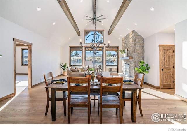 dining area with high vaulted ceiling, ceiling fan with notable chandelier, a fireplace, beam ceiling, and light hardwood / wood-style flooring