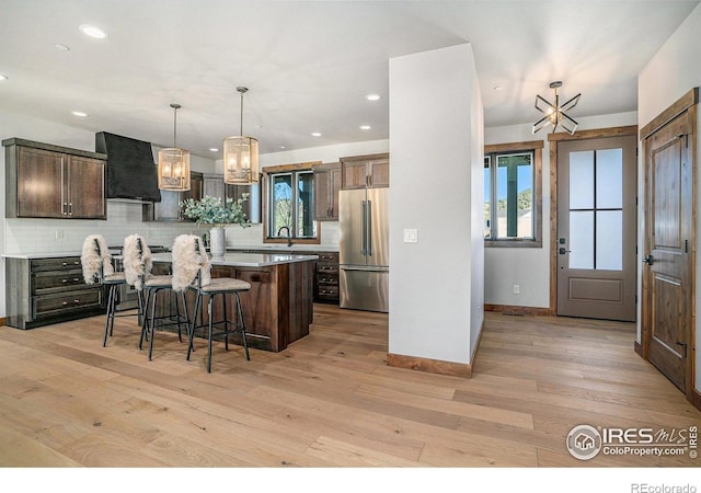 kitchen with backsplash, a center island, light hardwood / wood-style flooring, wall chimney range hood, and high end fridge