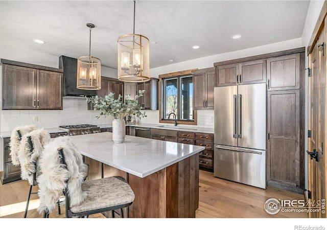 kitchen with hanging light fixtures, a kitchen island, dark brown cabinets, appliances with stainless steel finishes, and light hardwood / wood-style floors