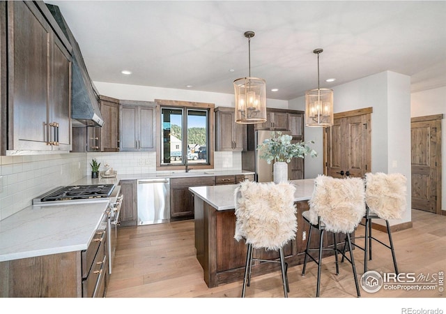 kitchen featuring decorative light fixtures, appliances with stainless steel finishes, light hardwood / wood-style floors, and a kitchen island