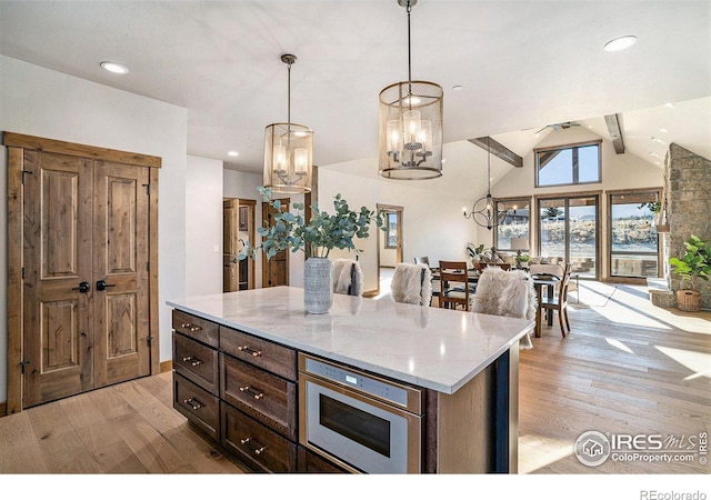 kitchen featuring light stone counters, pendant lighting, light hardwood / wood-style flooring, lofted ceiling with beams, and a center island