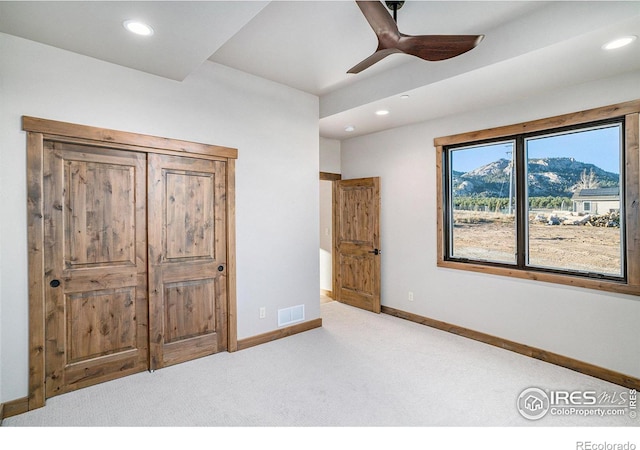 unfurnished bedroom featuring a mountain view, ceiling fan, and light colored carpet